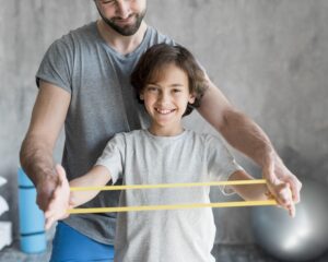 PT assisting a boy in theraband arm exercise Click to go to our Physical Therapy Treatment page