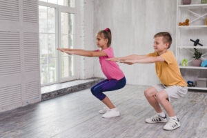 2 children participating a group fitness class working on strength through chair pose.